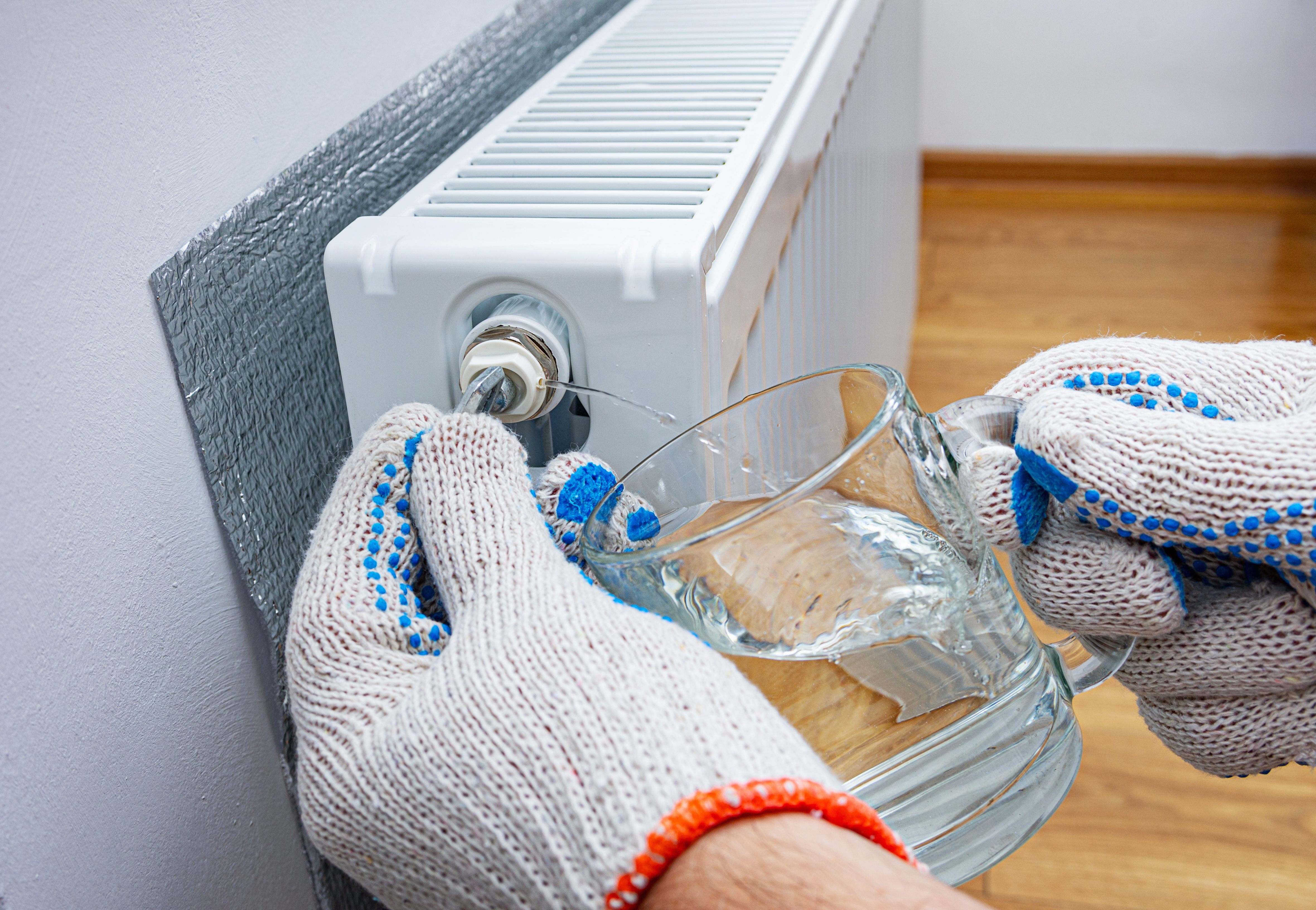 HVAC technician using a manifold gauge to check refrigerant levels on an outdoor air conditioning unit with exposed wiring and components.